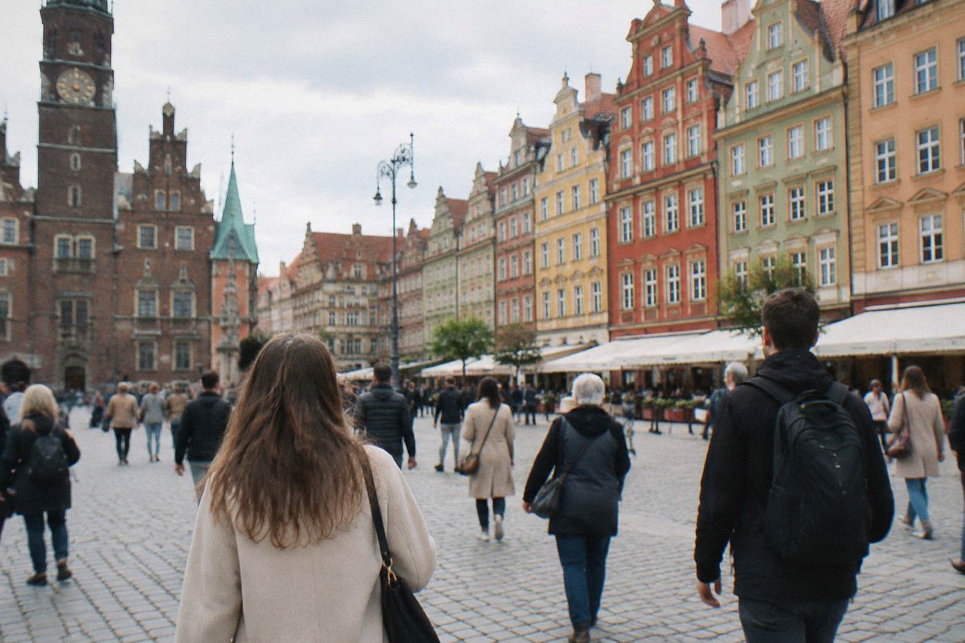 Visitors walking across Wroclaw's market square past colorful townhouse facades on a bright day