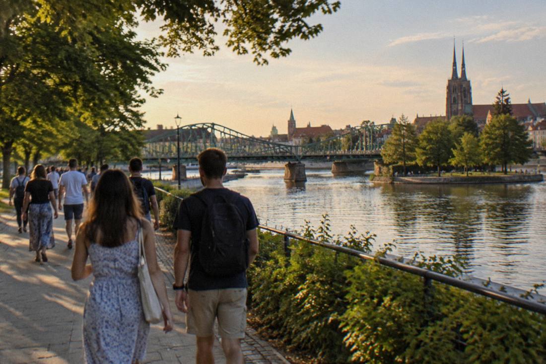 Tourists strolling along a tree-lined path beside the Odra river in Wroclaw on a summer afternoon