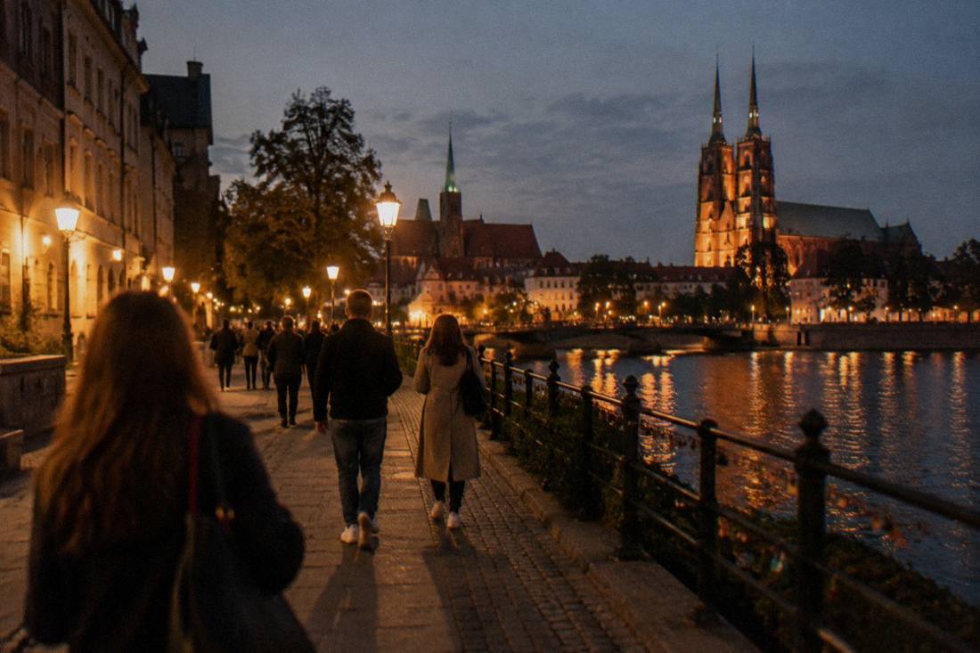 People walking along a lit riverside promenade in Wroclaw at night