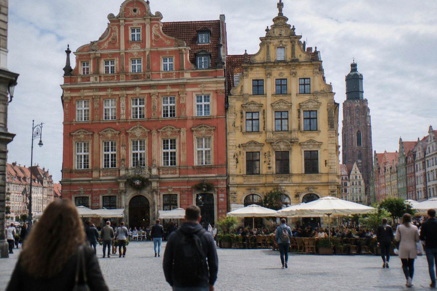 Two ornate townhouses lining Wroclaw's Market Square on a bright day, with café tables and pedestrians below