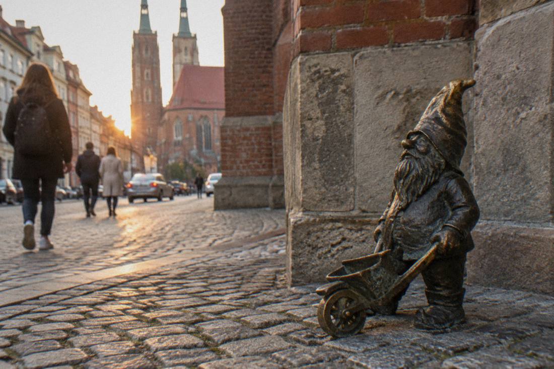 A bronze dwarf statue fixed to a cobblestone street beside an old church wall