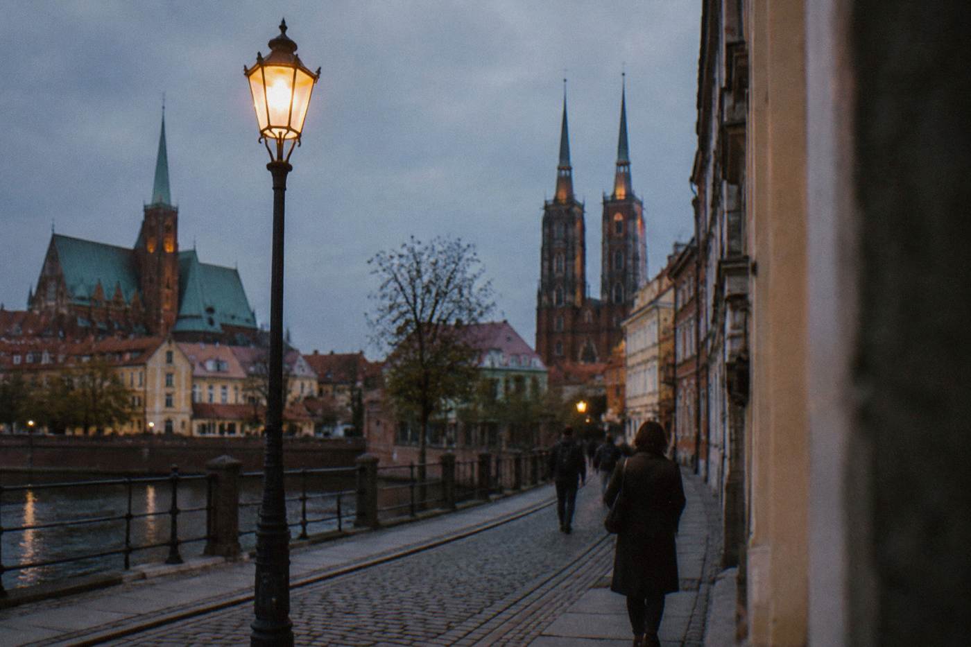 A hand-lit street lamp glowing at dusk in a historic European square