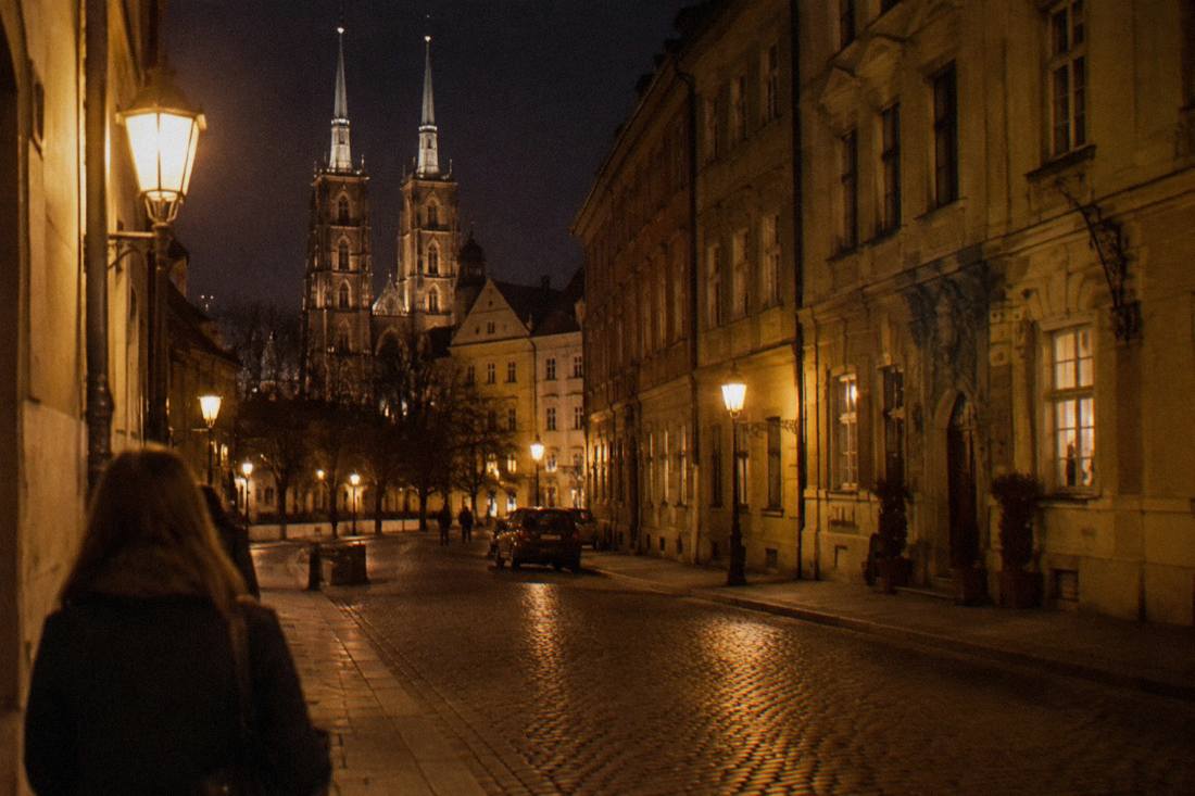 Warm light from old gas lamps along an empty cobbled street at night