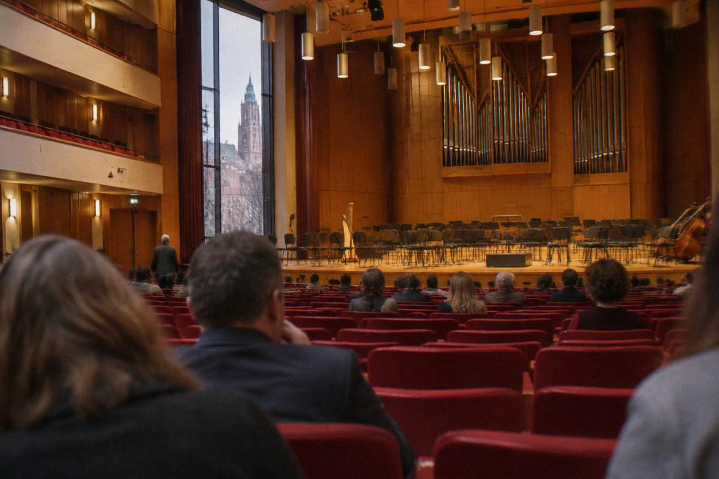 A concert hall interior with rows of red seats facing an empty stage under warm lighting