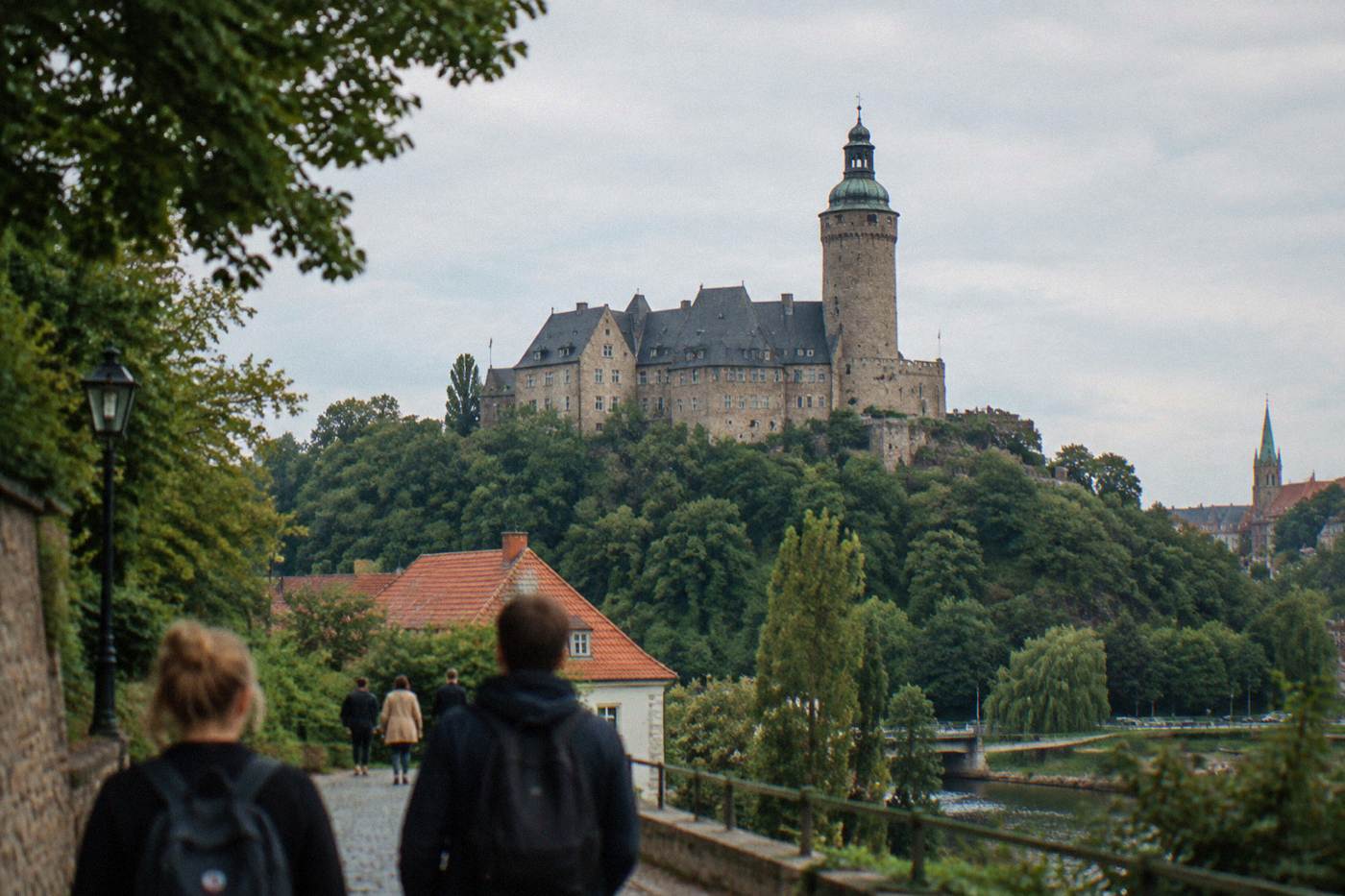 A large stone castle with a tall tower rising above green forested hills