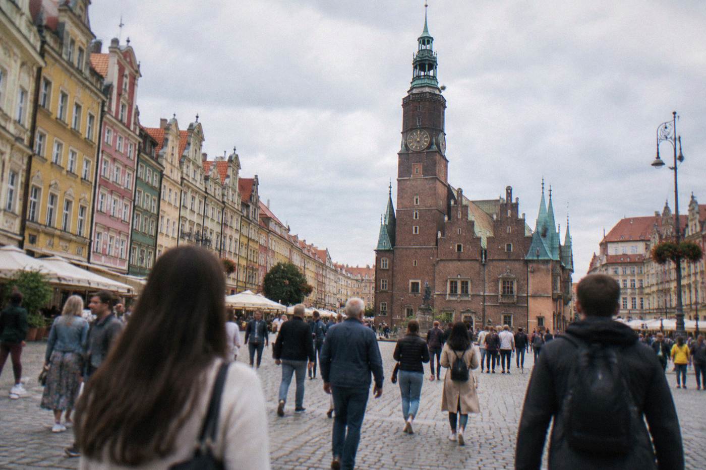 Visitors walking across Wroclaw Market Square with the Gothic town hall on one side and pastel townhouses behind.