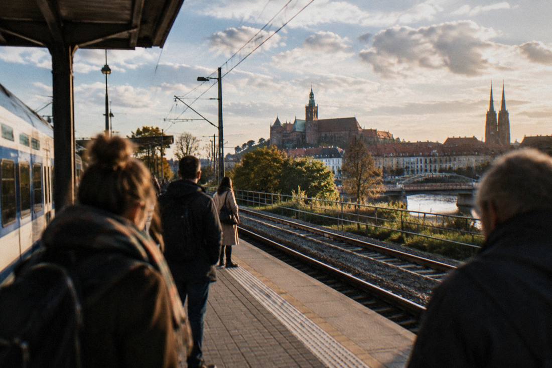 A regional train platform in Lower Silesia with a castle hill visible in the distance under a partly cloudy sky.
