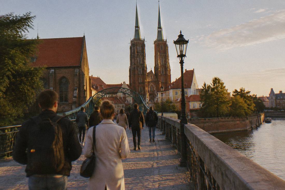 Visitors crossing a stone bridge toward cathedral towers on Ostrow Tumski