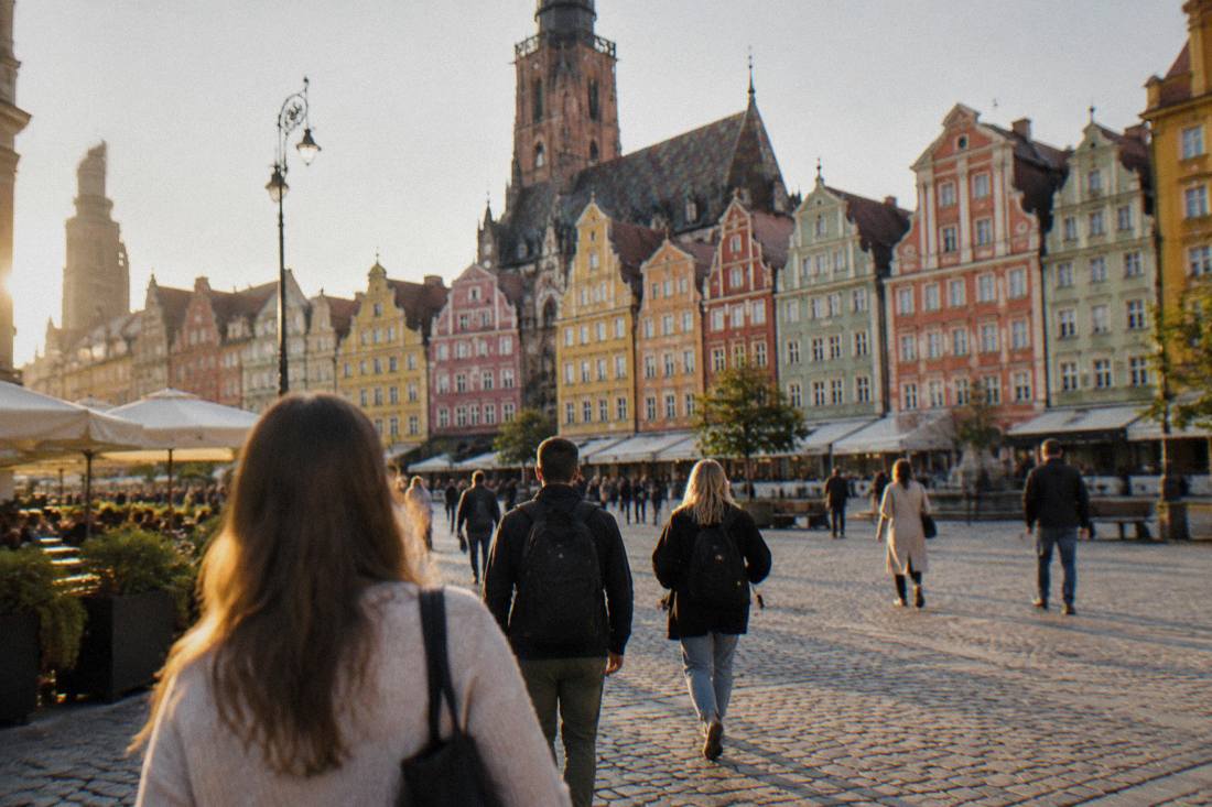 Travelers walking across a historic European market square lined with colorful townhouses