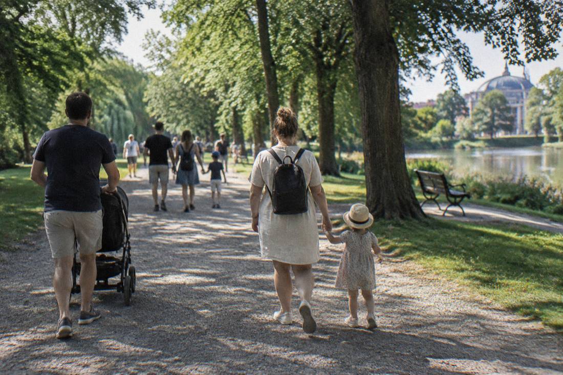 Families walking a wide gravel path under large trees in Szczytnicki Park in Wroclaw