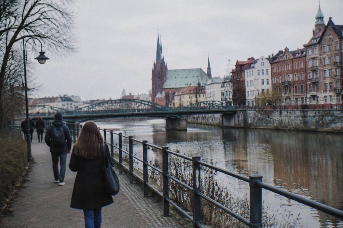 A riverside path along a city river with bridges and old buildings in the background