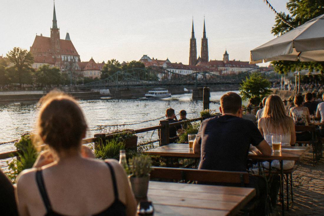 A summer beer garden with tables along the Odra riverbank near one of the central bridges