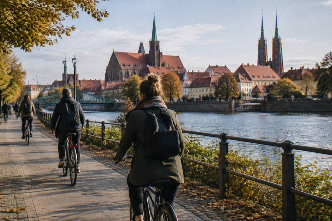 Cyclists riding a riverside path along the Odra with old town rooftops behind them