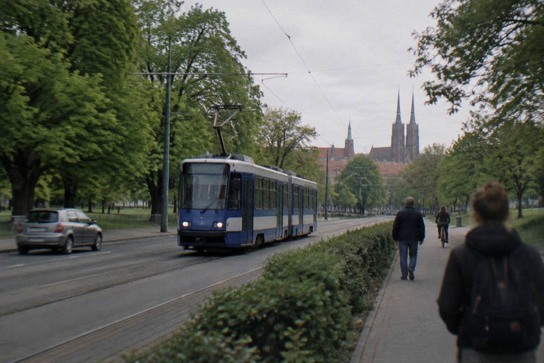 A tram passing green trees on a street heading toward Wroclaw's eastern parks