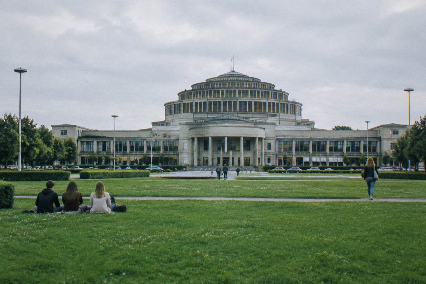 A vast domed concrete hall with symmetrical wings seen from a wide green lawn