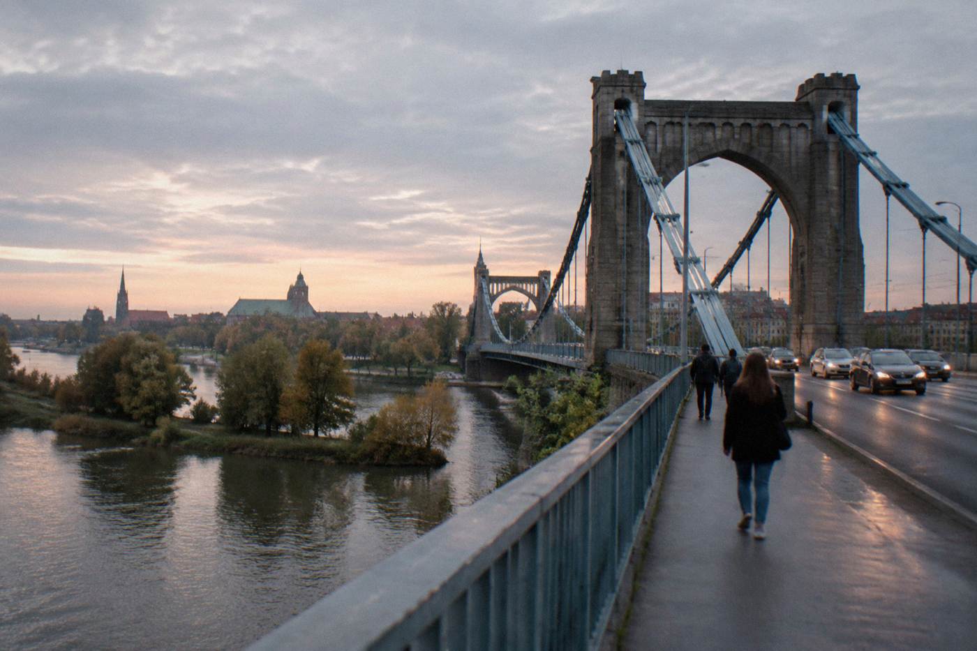 A steel suspension bridge spanning the Odra river with church towers visible across the water in Wroclaw