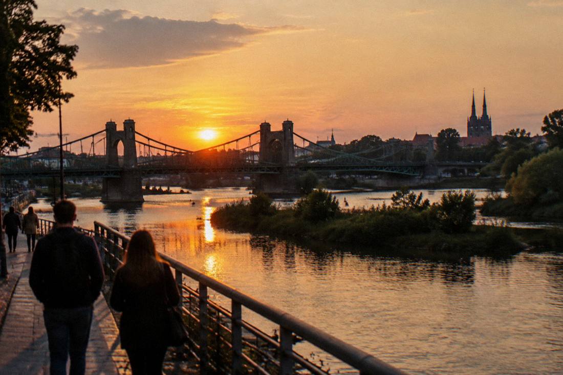 Sun setting behind a bridge silhouette with river water reflecting orange light