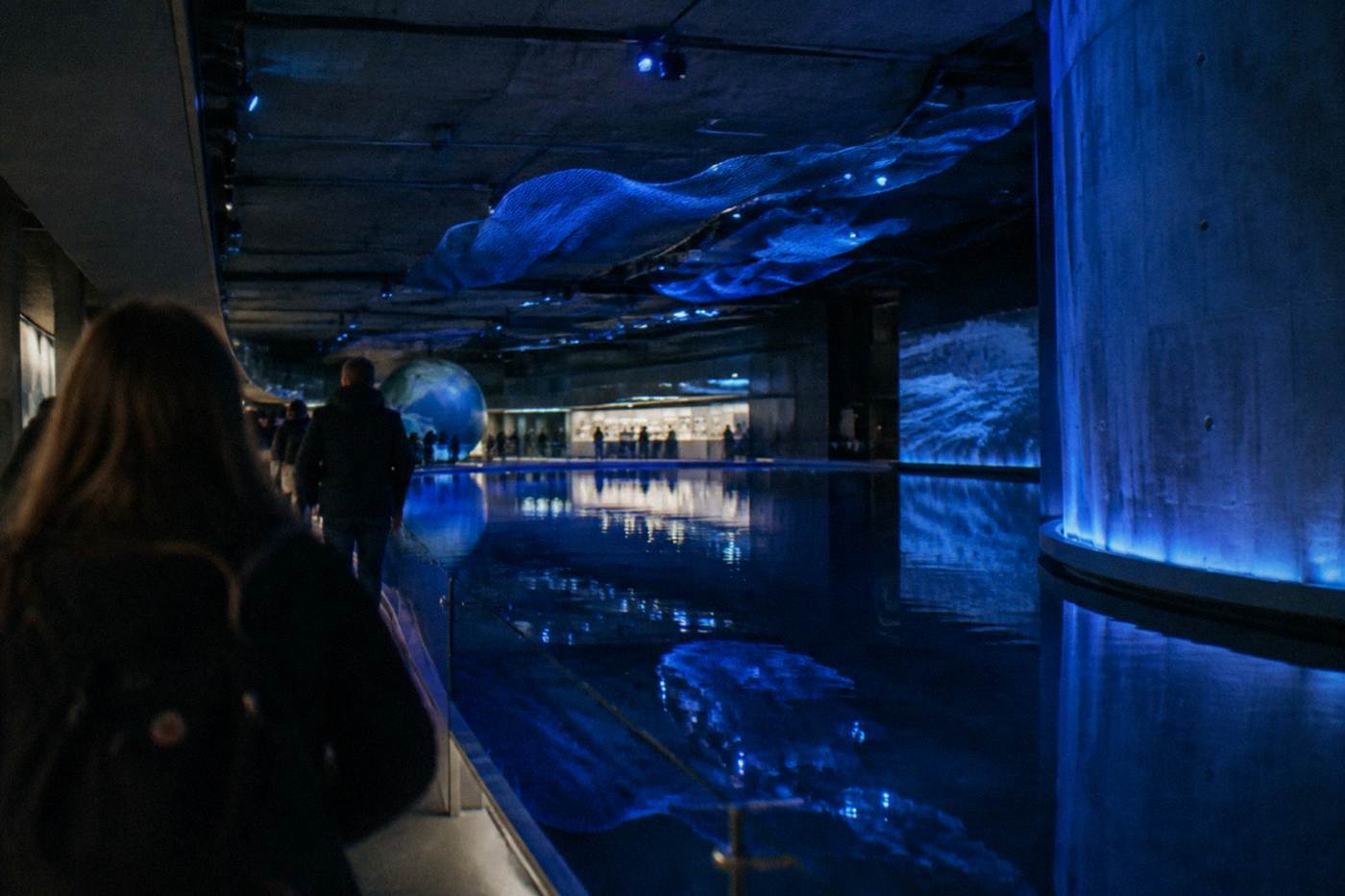 Underground museum hall with deep blue lighting and a still pool of water reflecting the ceiling