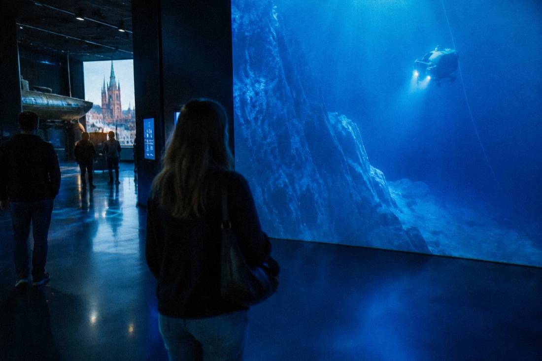 A projected ocean depth display lighting a dark exhibition room in shades of blue