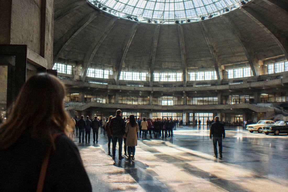 A historic concrete domed hall with visitors gathered at its center beneath a large skylight
