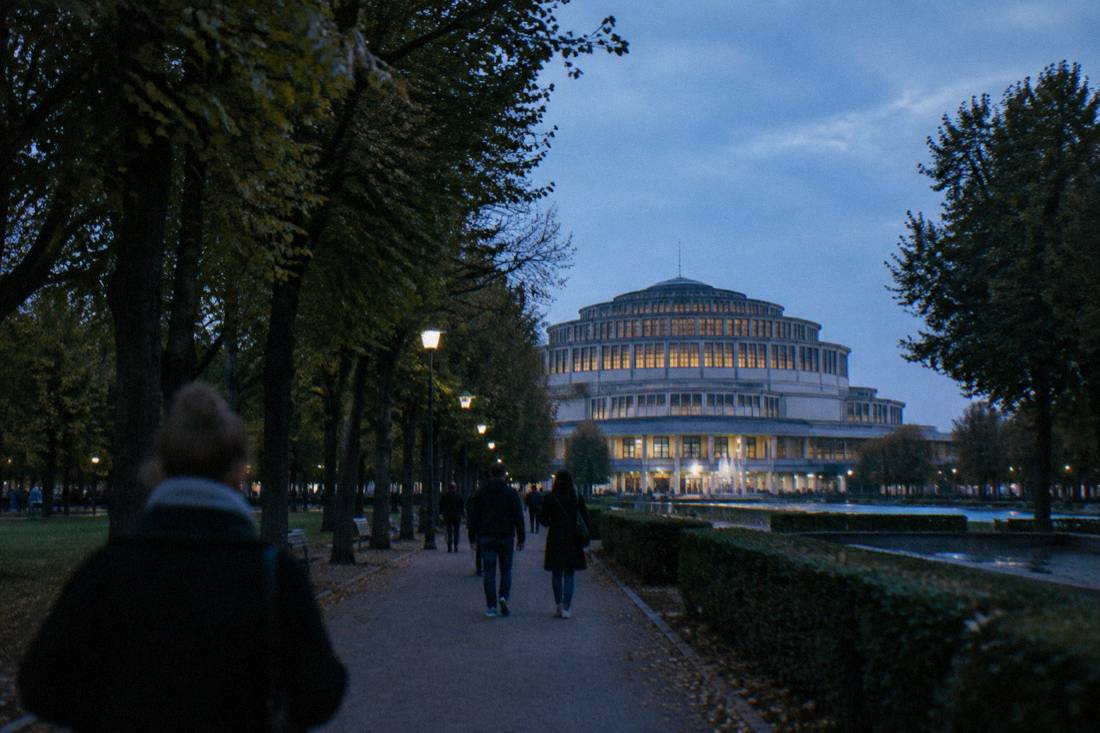 A tree-lined park avenue in Wroclaw leading toward the Centennial Hall dome