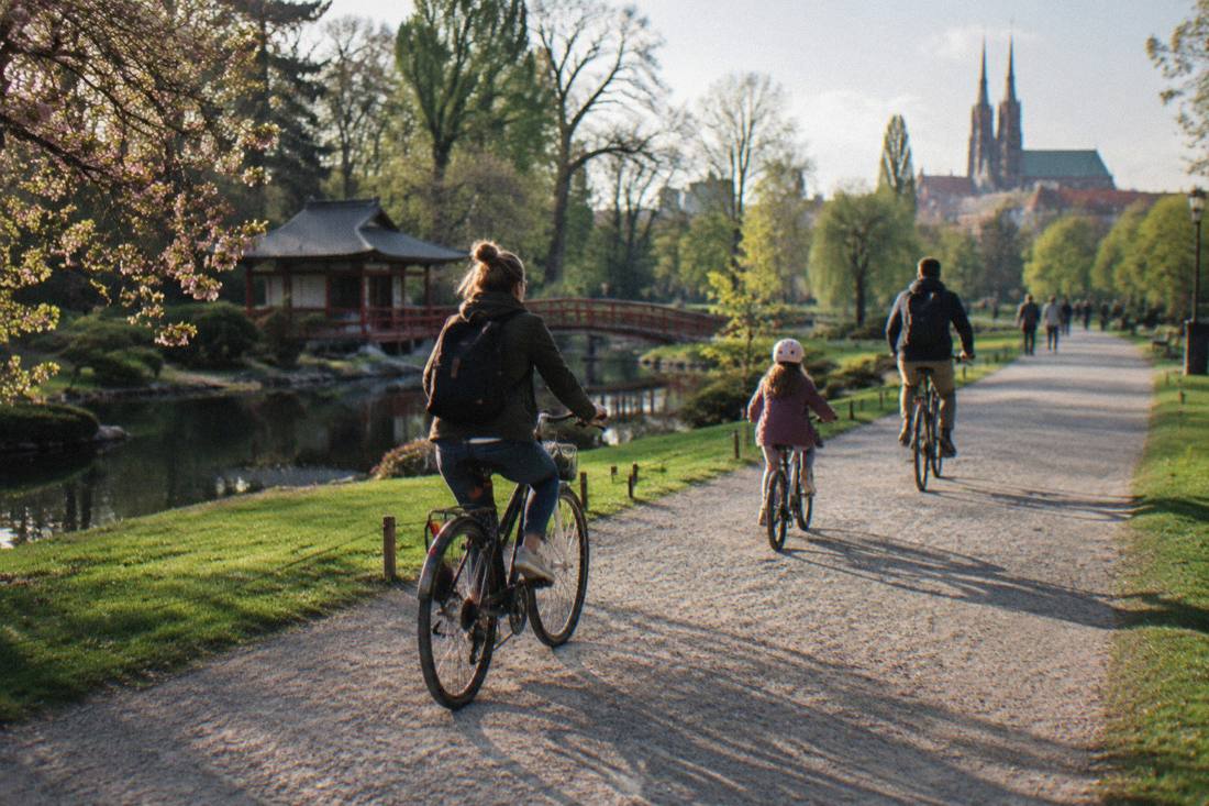 A family cycling on a broad gravel path beside lawns in Szczytnicki Park in Wroclaw