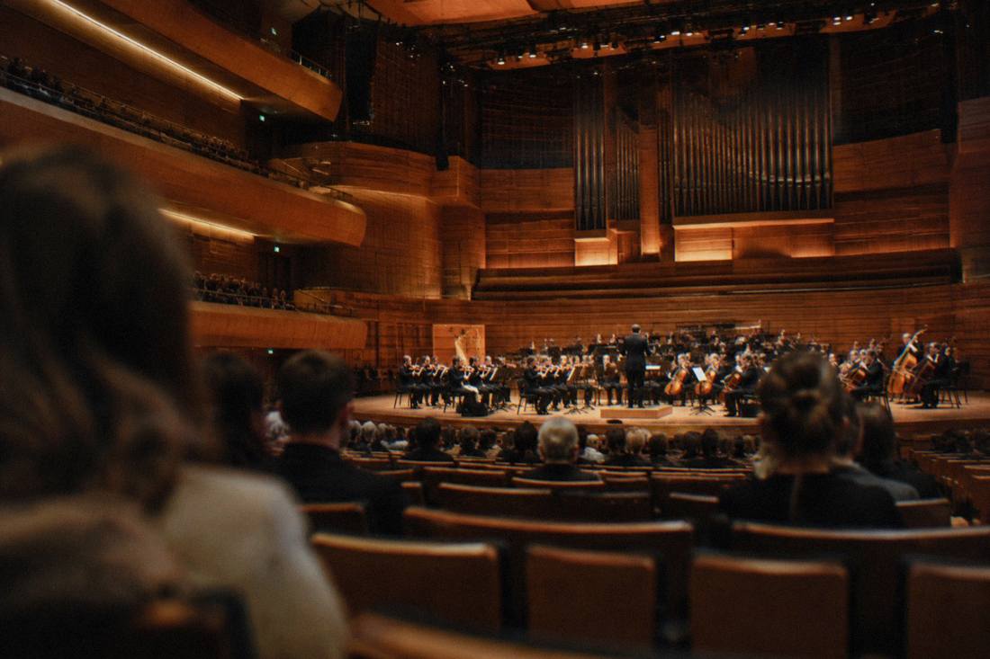 Concert hall interior with rows of seats facing an orchestra stage under warm lighting
