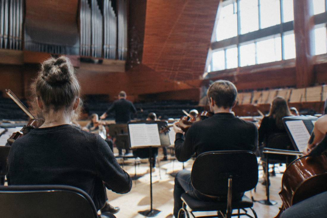 Musicians warming up on a concert hall stage with music stands and chairs