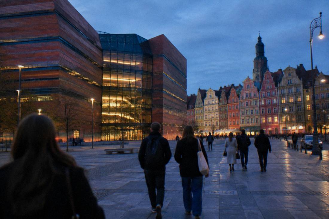 Visitors walking across Wroclaw's market square toward colorful townhouses at dusk