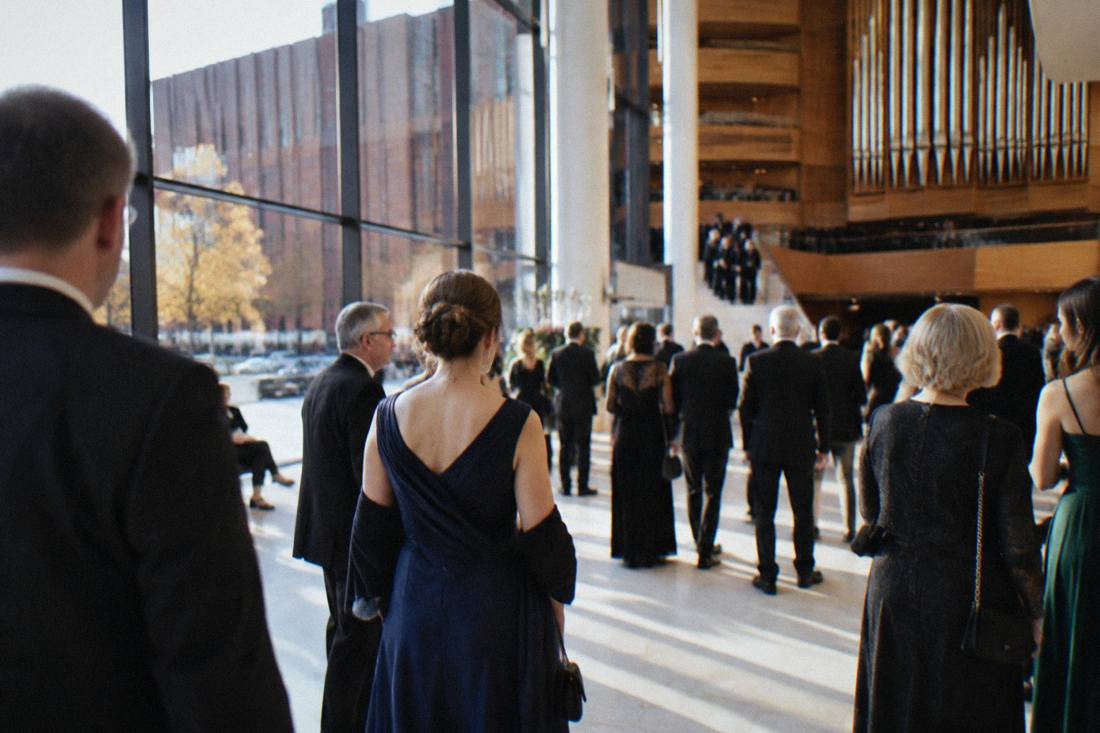 Audience members in evening dress gathering in a bright concert hall foyer before a performance