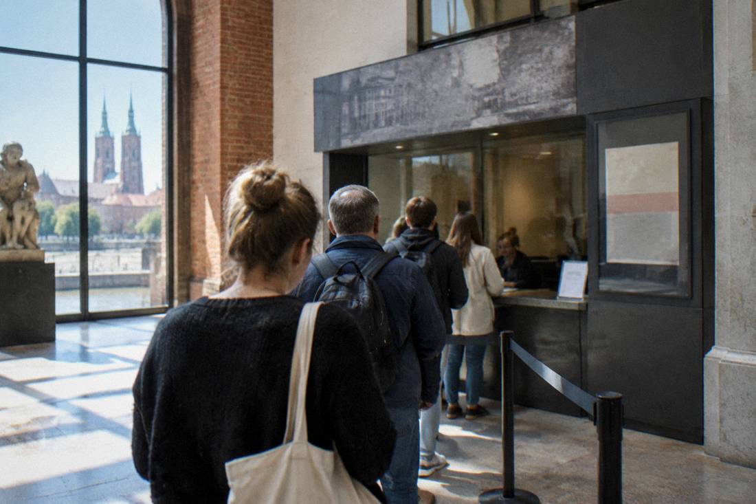 A museum ticket desk in Wroclaw with price signage and a short queue of visitors