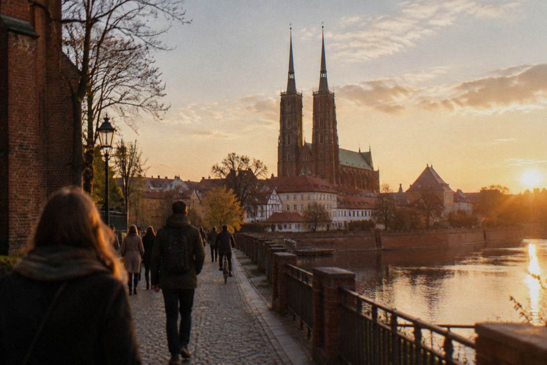 Twin cathedral spires seen from a riverside path in late afternoon light