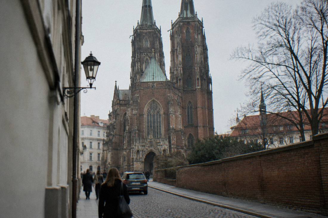 A stone church facade with gothic details seen from a narrow street
