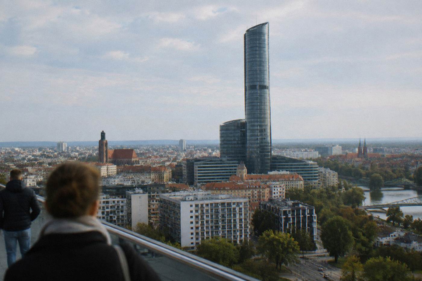 A tall glass skyscraper rising above lower city blocks on a clear afternoon