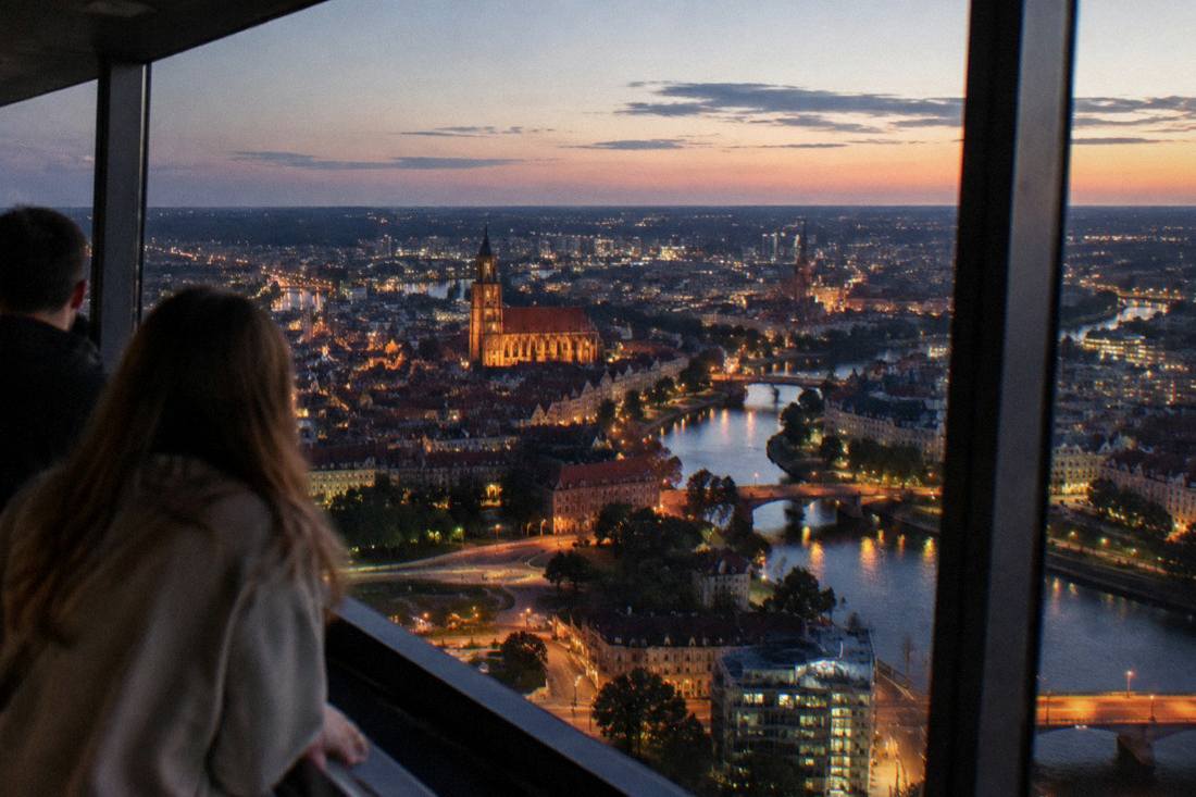 Evening city lights spreading across rooftops and river bends seen from above