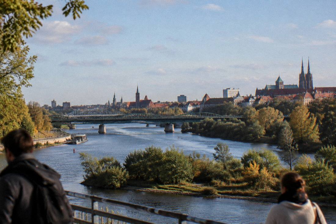A city skyline seen across a wide river with several bridges, green islands in the foreground and church towers in the distance