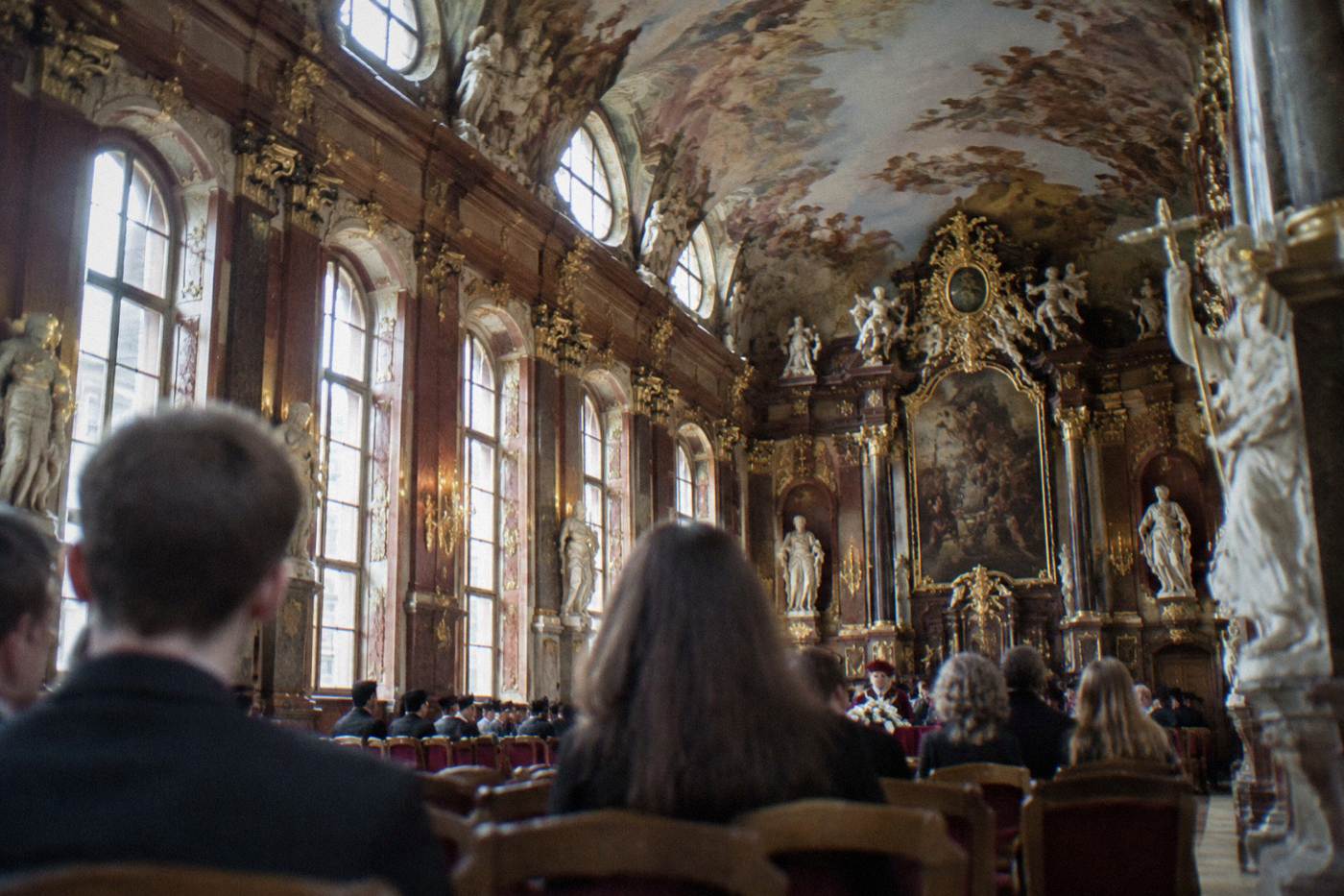 The ornate gilded interior of a baroque university ceremonial hall with statues and a painted ceiling