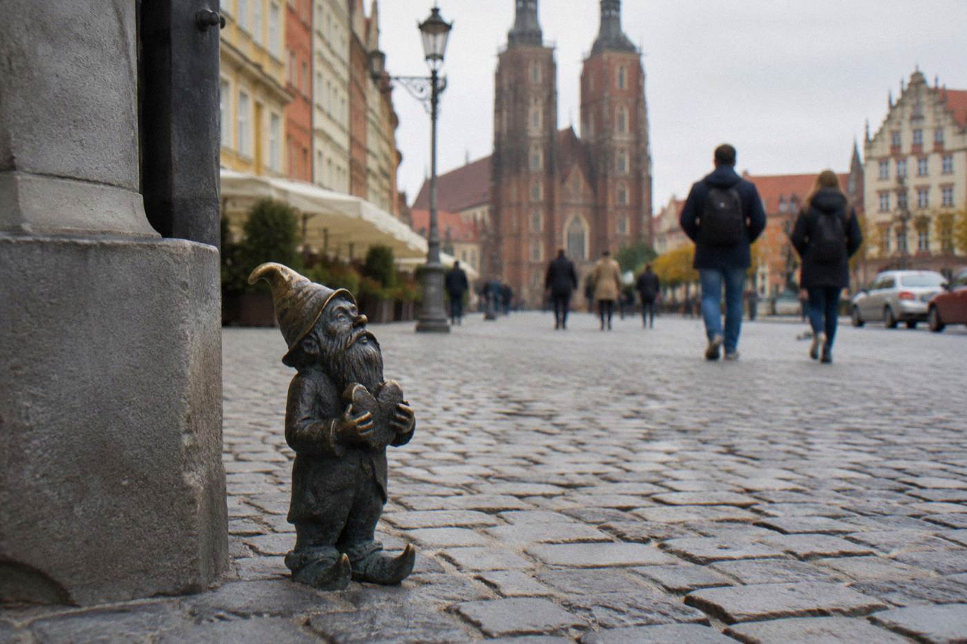 A small bronze dwarf statue standing on a cobblestone street in Wroclaw's old town