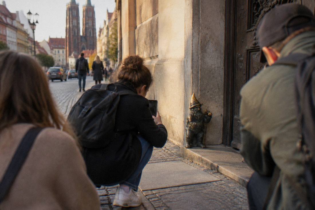 Tourists crouching to photograph a tiny bronze dwarf on the edge of a stone doorway