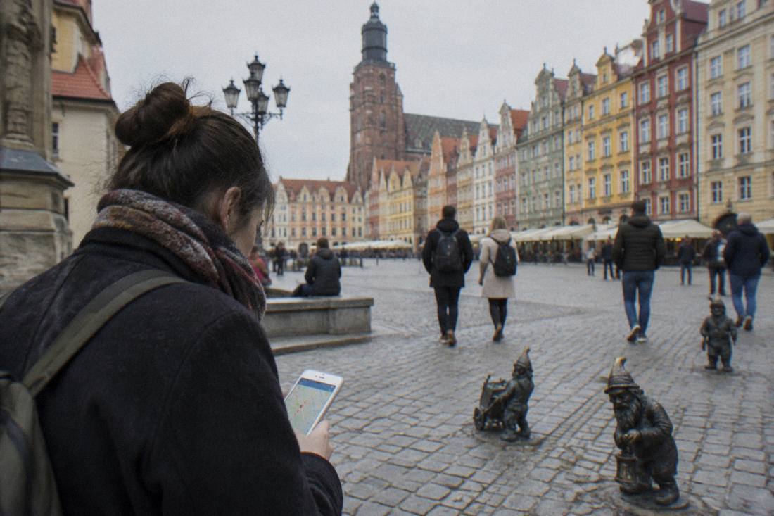 A visitor consulting a phone map while standing on a cobbled square surrounded by historic townhouses