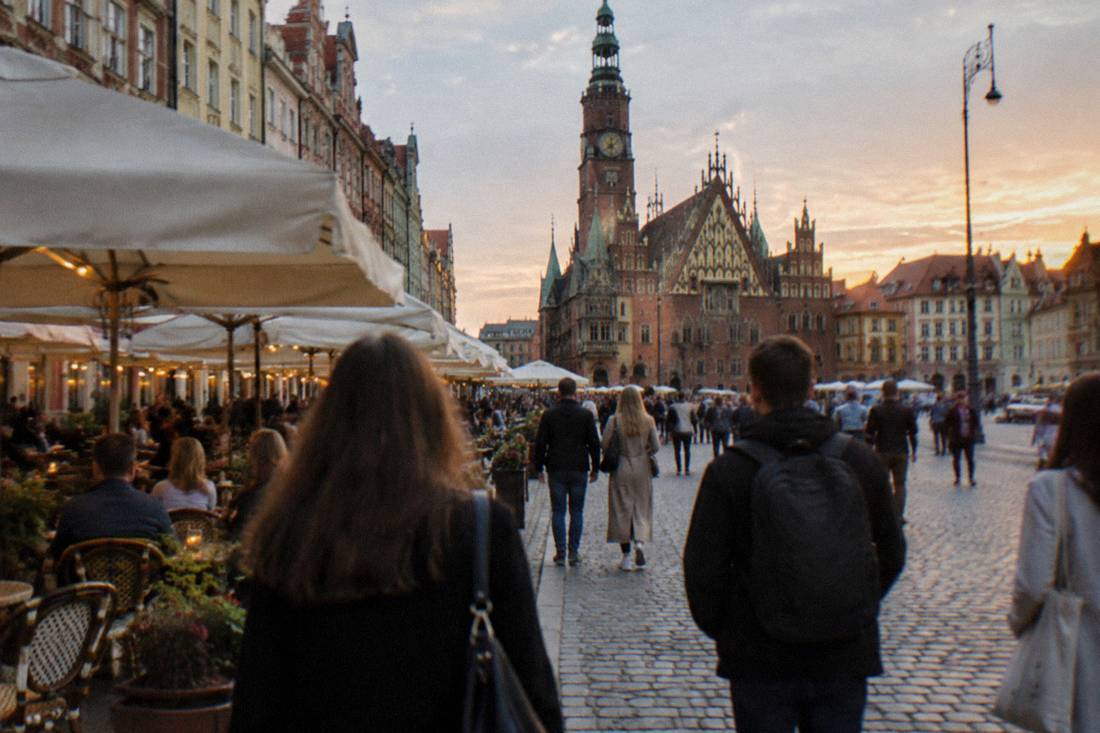 People strolling between outdoor cafe tables in a pedestrian square at dusk