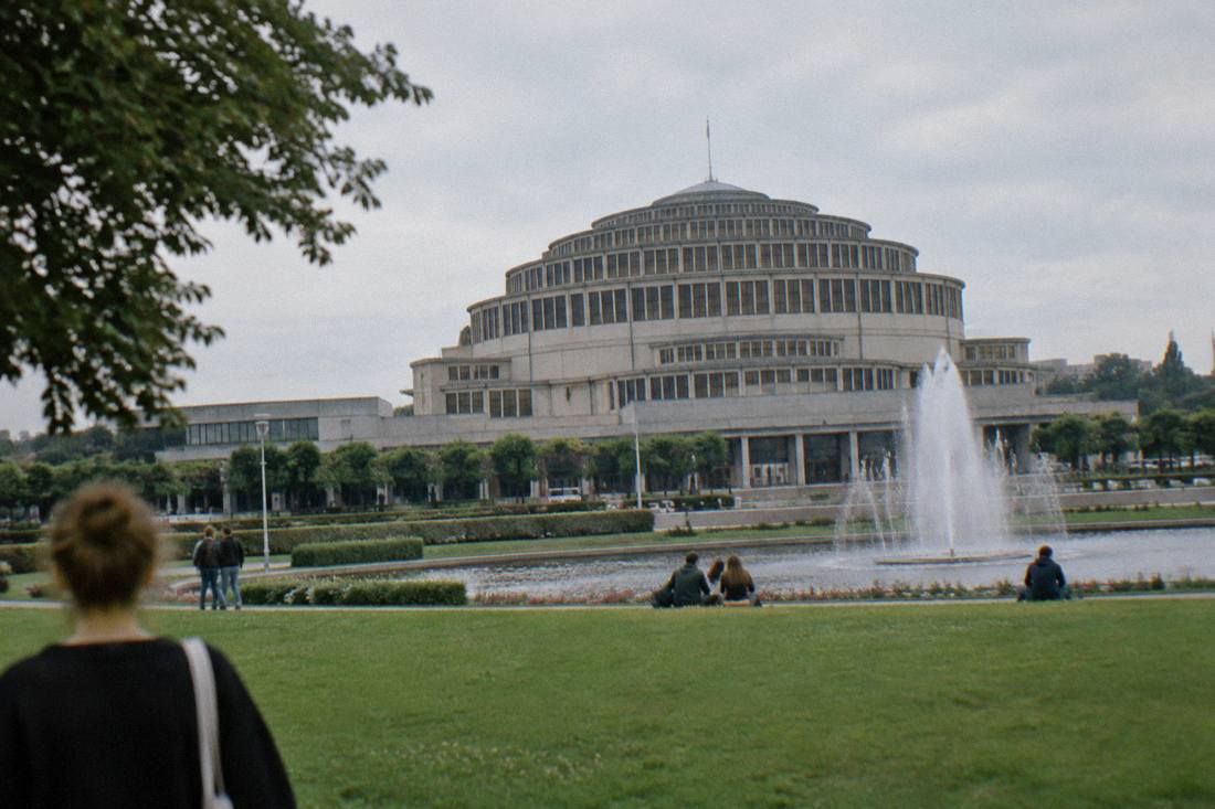 A large reinforced concrete domed exhibition hall seen across a park lawn with a fountain