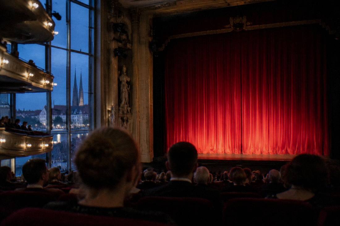 A red theater curtain glowing under stage lights before an evening performance