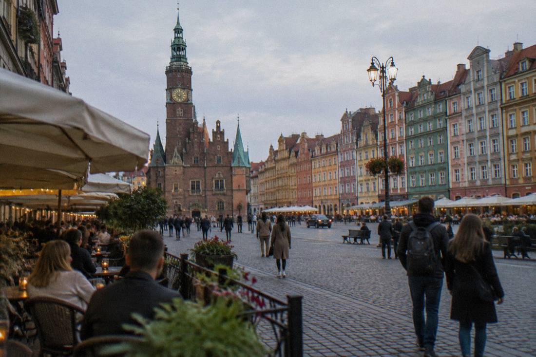 Cafe tables and painted townhouses around a large old market square in the evening