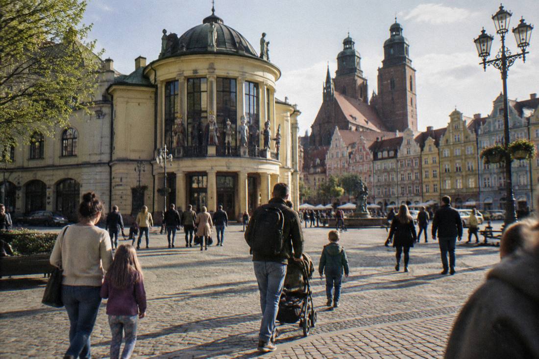 Families strolling across Wroclaw's market square on a bright afternoon