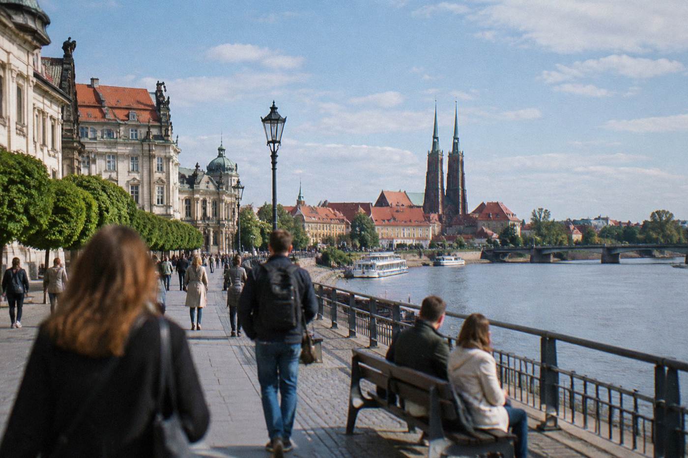 A wide river promenade lined with baroque buildings under a blue sky