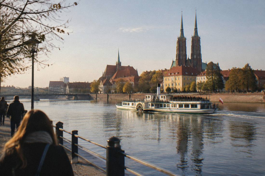 A paddle steamer boat on a wide river passing city buildings