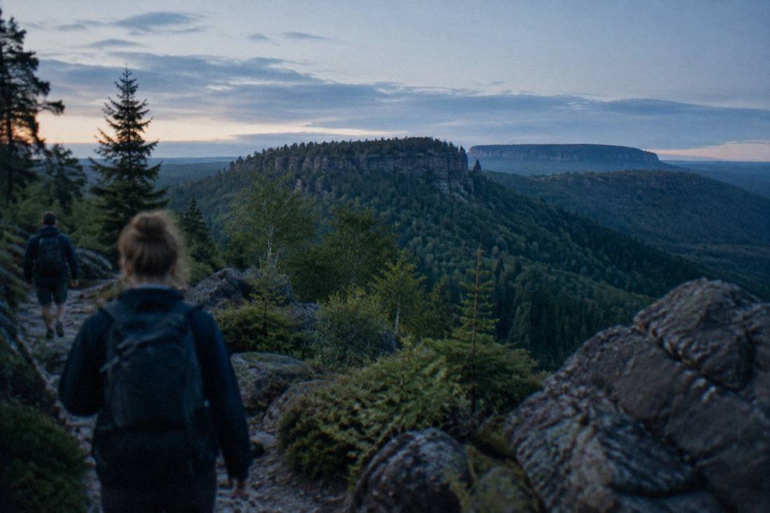 A green forested ridge under soft morning light with rock outcrops along the trail