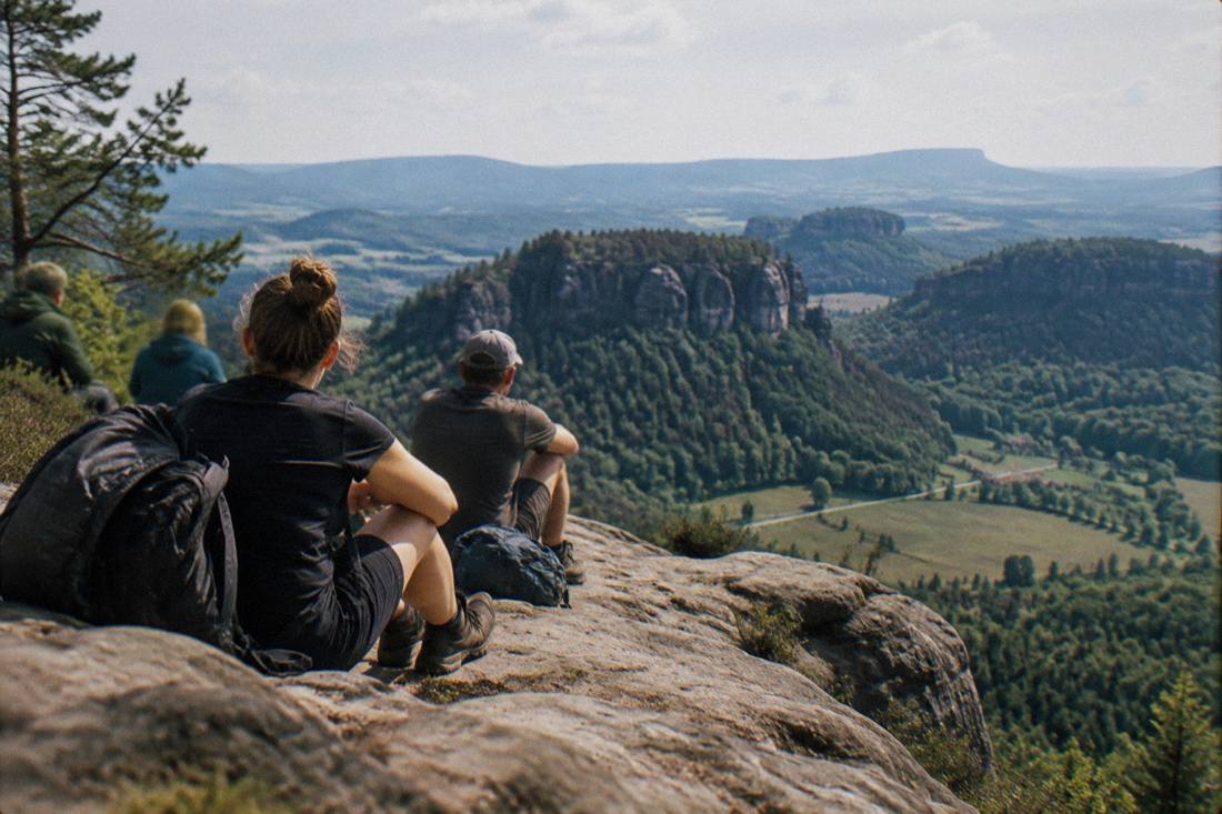 Tired hikers sitting on a sunlit sandstone ledge above a wide green valley