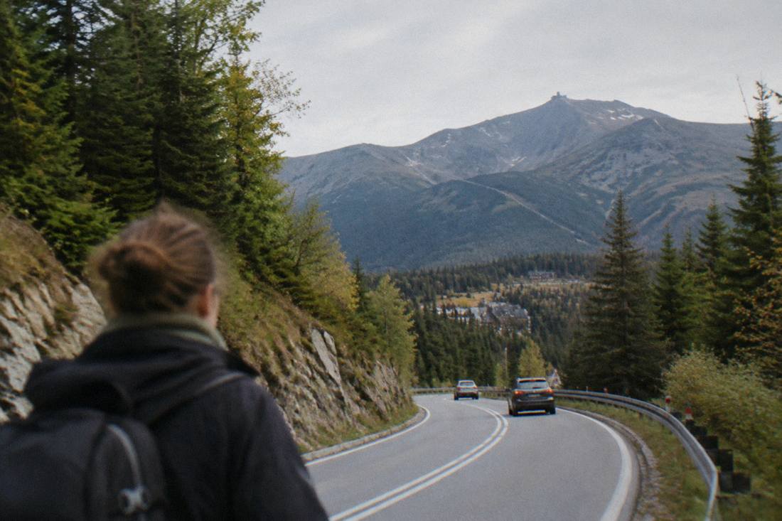 A winding mountain road through forested foothills toward high peaks